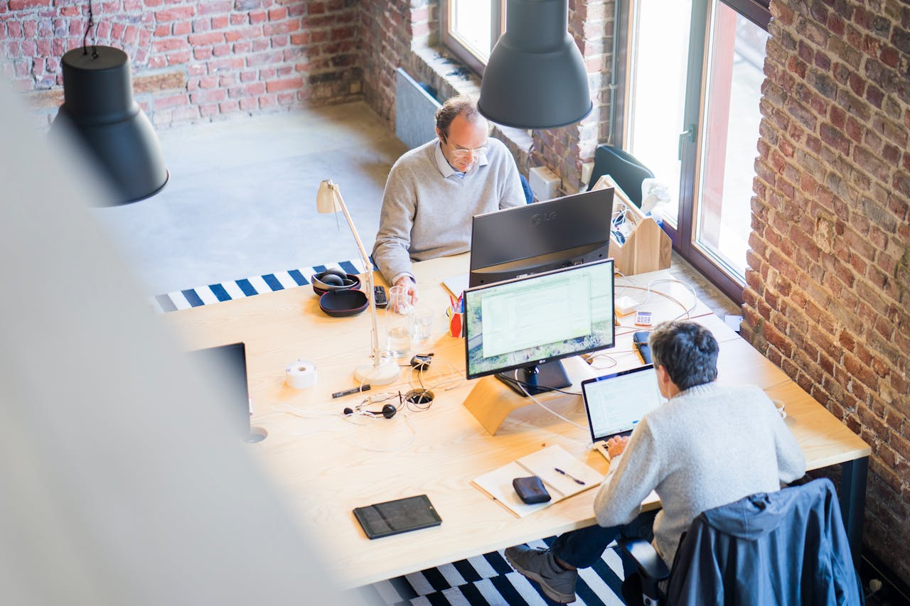 Two men seated at a large desk at their computers in an open floor plan office space