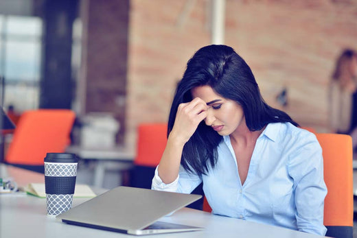 A stressed woman in a modern office with a laptop and coffee, reflecting challenges in different types of work environments