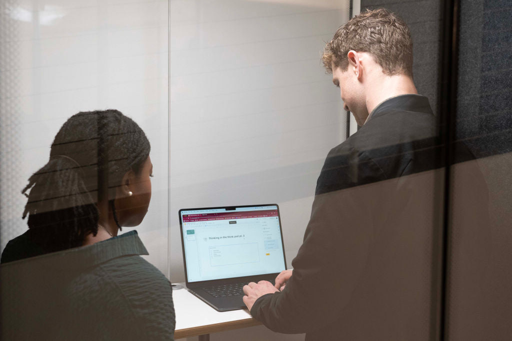 A man and a woman meeting and working at a laptop inside a 2 person Booth