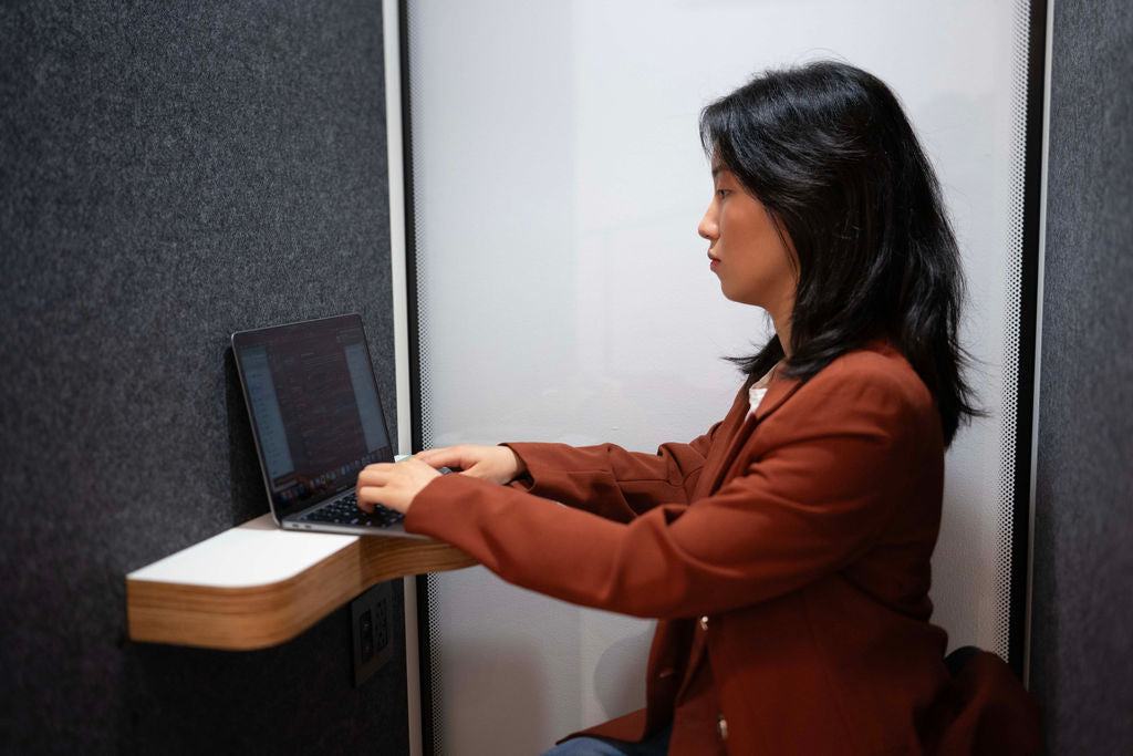 A woman seated at her laptop typing on a desk inside the 1 Person Booth